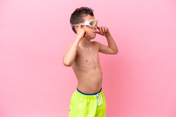 Little caucasian boy wearing a diving goggles isolated on pink background having doubts and thinking