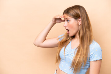 Fototapeta premium Young caucasian woman isolated on beige background with surprise expression while looking side