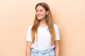 Young caucasian woman isolated on beige background looking to the side and smiling