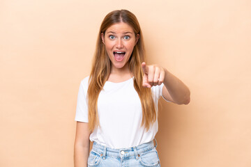 Young caucasian woman isolated on beige background surprised and pointing front