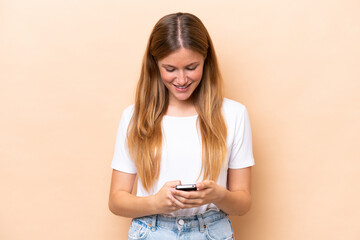 Fototapeta premium Young caucasian woman isolated on beige background sending a message with the mobile