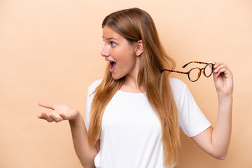 Fototapeta premium Young pretty blonde woman with glasses isolated on beige background with surprise facial expression