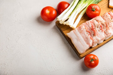 Board with pork fat, green onions, homemade bread and cherry tomatoes on a gray stone background. Salo. Delicious salty lard with pepper. Space for copy. Space for text.