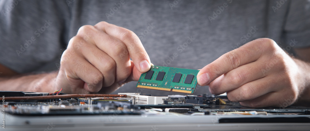 Wall mural technician installing random access memory on laptop computer.
