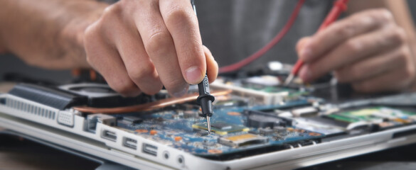 Technician hand checking motherboard with multimeter.