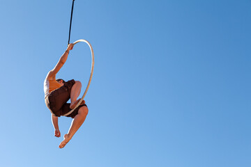 a young trapeze artist suspended in mid-air attached to a circus hoop
