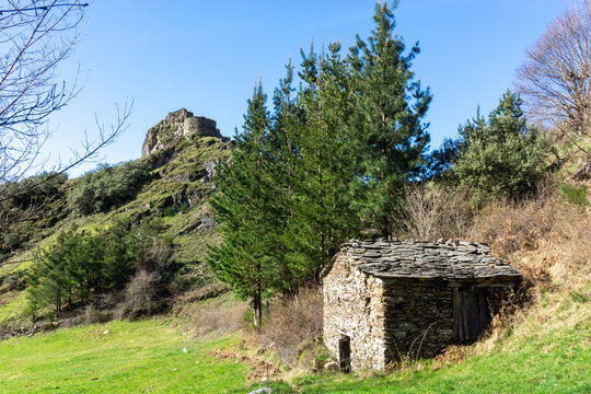 Cabaña de pastores de piedra en la Sierra do Courel, al fondo de una colina, las ruinas del castillo de Carbedo. Folgoso do Courel, Lugo, Galicia, España.