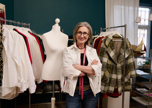 Senior female fashion designer near new collection of women clothes and tailoring mannequin in a fashion clothing design workshop
