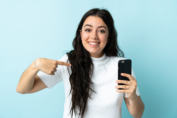 Fototapeta premium Young woman using mobile phone isolated on blue background with surprise facial expression