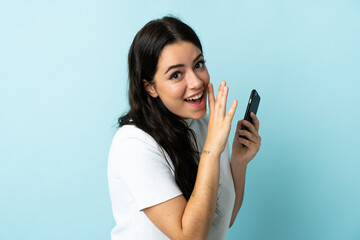 Young woman using mobile phone isolated on blue background whispering something