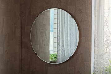 one large round glass mirror with reflection hangs on a brown wall in the room