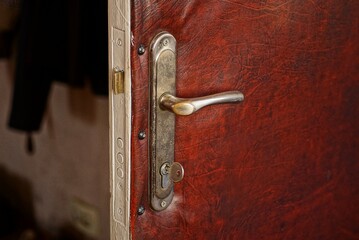 gray metal door handle and door lock with a key in the door on red leather in the room