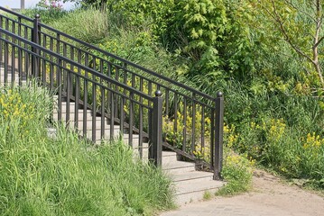 part of a staircase with concrete steps and black iron handrails outdoors in green grass and yellow flowers