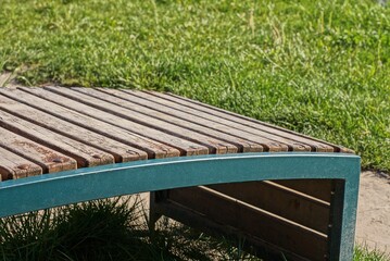 Fototapeta premium one empty brown wooden bench stands in green grass by a gray earth in a park