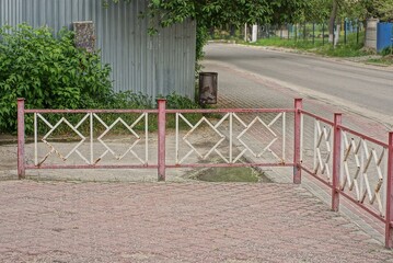 red white metal decorative fence made of twigs on a sidewalk near an asphalt road