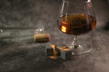 transparent whiskey with a bottle and a wooden cork on a dark background. whiskey stones in a glass