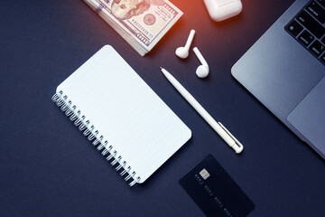 Online business, freelance or working at home concept with empty white notepad, pen, credit card, laptop and headphones on a dark background.