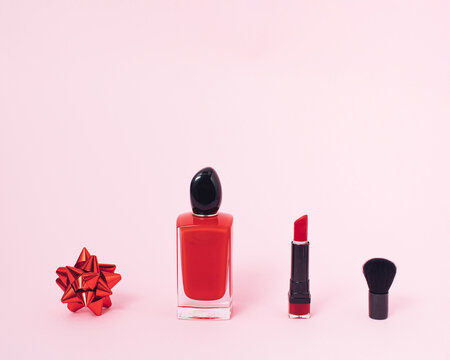 Minimal layout of women's gift idea like perfume, lipstick, makeup brush and red ribbon on pastel pink background. Creative concept of giving with copy space for greeting message as present.