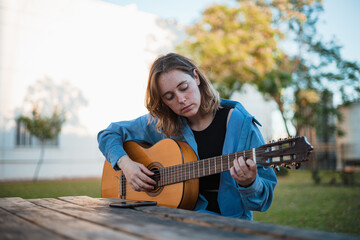 Young woman composing a song with her guitar while sitting on a wooden picnic table