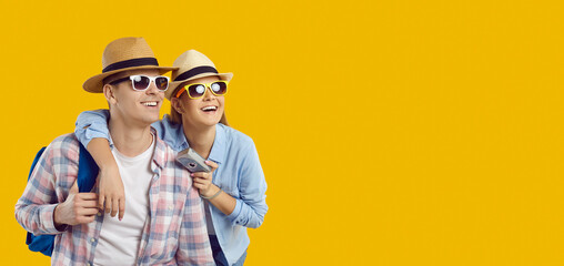 Fototapeta Amazed joyful young couple of tourists enchanted looking at copy space on orange background. Smiling young man and woman in casual clothes, sunglasses, summer hats and with camera in hand enjoy tour. obraz