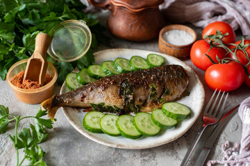A hearty lunch for the whole family:baked mackerel with herbs and vegetables on a plate on a gray background. Fish baked with vegetables on a beautiful dish. Close-up