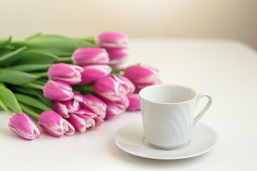 Fototapeta na wymiar a white mug and a bouquet of beautiful pink tulips on white table