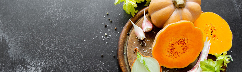 Banner vegetables on cutting board: orange squash, celery, garlic and spices - pepper. salt. Black background. Copy space