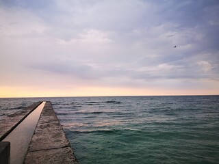 View of the Black Sea from the beach of Odessa (Ukraine). Calm sea, a seagull sits on a breakwater against the backdrop of dawn over the water. Tourist place, recreation area