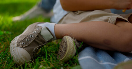 Unknown boy legs seat on blanket close up. Little kid rest on green park.