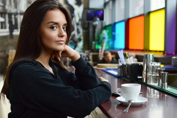 Beautiful brunette girl drinks tea or coffee in a cafe. Beauty model woman with a cup of hot drink.