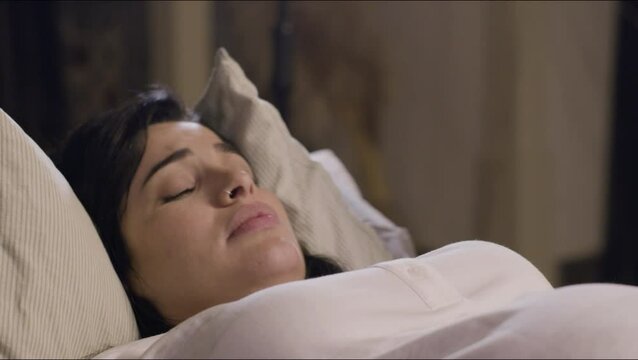 Woman lying on bed and giving birth at home. Medium shot of crying woman, holding her husband hand, having contractions and suffering from pain. Childbirth, motherhood, family concept