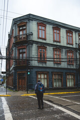 Fototapeta na wymiar Backpacker crossing street and beautiful green old centuries three stored building with neoclassical architecture, ornaments and balconies in a cloudy day, Valdivia, Chile