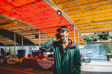 Young, bearded, handsome and happy guy with green jacket talking on the phone in the public 'Mercado Fluvial' (river market), Valdivia, Chile
