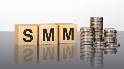 SMM - text on wooden cubes on a cold grey light background with stacks coins