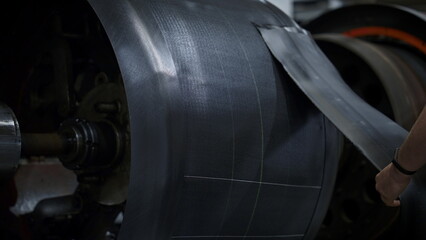 Tyre factory worker hands setting new rubber tape on industrial workshop machine
