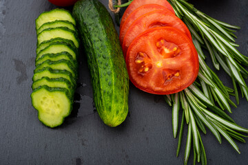 Vegetable table. Cucumbers, tomatoes and rosemary on a black table
