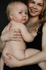 Portrait closeup of young smiling mother holding on hands cute naked baby on black background....