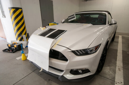 Installation (gluing, applying) of black strips decal of glossy black foil on a white sports muscle car in a garage.