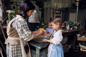 Family of mother and little sisters bathing little ducklet in old village
aluminum bath can in terrace. Two little baby girls of 3-years-old and 5-years-old in retro vintage dresses play with ducklet