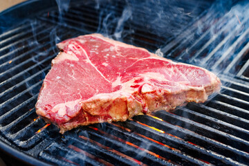 Raw dry aged wagyu porterhouse beef steak grilled as close-up on a charcoal grill with fire and...