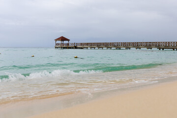A pier goes into the sea,at the end there is a gazebo.The blue sea water and the sky are separated by the horizon line,a pier.Caribbean Coast in the Dominican Republic.A wave runs over the sandy shore
