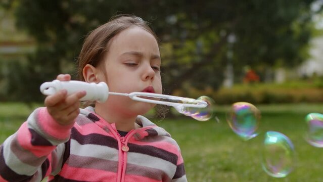  Little cute girl is playing outside blowing soap bubbles.
