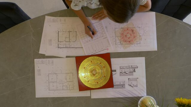 TOP DOWN: Young female analysing and making plan of feng shui for house building. Feng shui expert analysing energy flow distribution for balanced home and efficient house interior design arrangement.