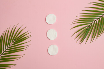 Fototapeta na wymiar Cotton pads and palm tree leaves on pink background. Summer beauty or spa concept. 