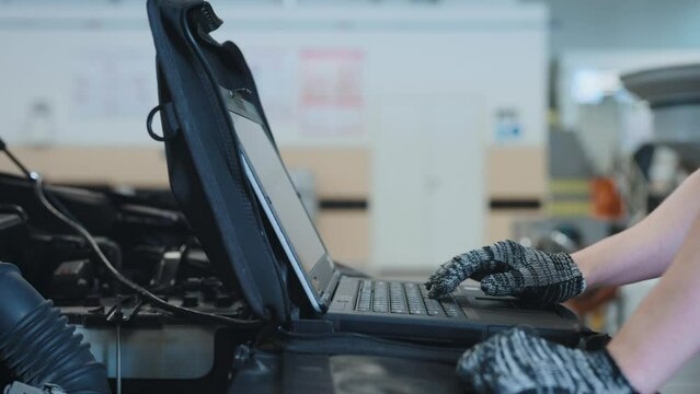 Car maintenance service. The mechanic makes diagnostics of the engine compartment using a computer.