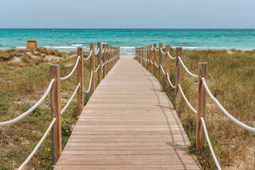 Fototapeta na wymiar Wooden platform through the sand dunes leading to the beach of the sea