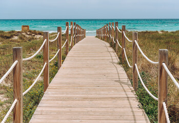 Obraz premium Wooden platform through the sand dunes leading to the beach of the sea