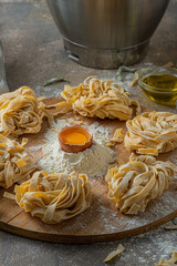 Freshly made tagliatelle pasta with eggs and flour on wooden board