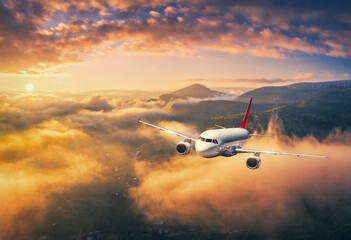 Fototapeta na wymiar Airplane is flying above the clouds at sunset in summer. Landscape with passenger airplane, mountains, orange sky. Aircraft is taking off. Business travel. Commercial plane. Aerial view. Transport