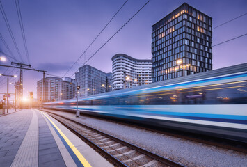 Hogesnelheidstrein in beweging op het treinstation bij zonsondergang. Bewegende blauwe moderne intercity passagierstrein, perron, gebouwen, stadslichten. Spoorweg in Wenen, Oostenrijk. Spoorvervoer